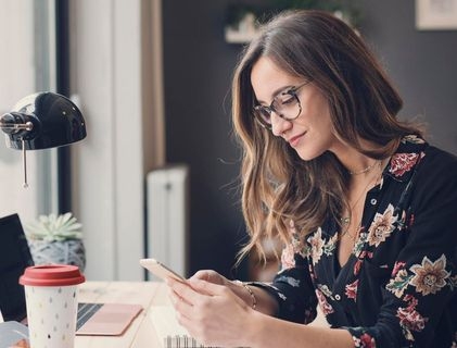 Junge Dame mit Handy sitzt am Schreibtisch
