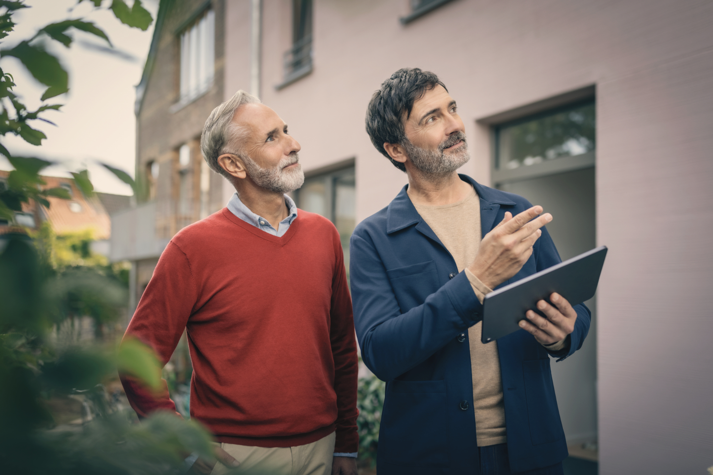 Ein Mann im blauen Sakko mit Tablet erkl&auml;rt einem &auml;lteren Herrn etwas an einem Geb&auml;ude