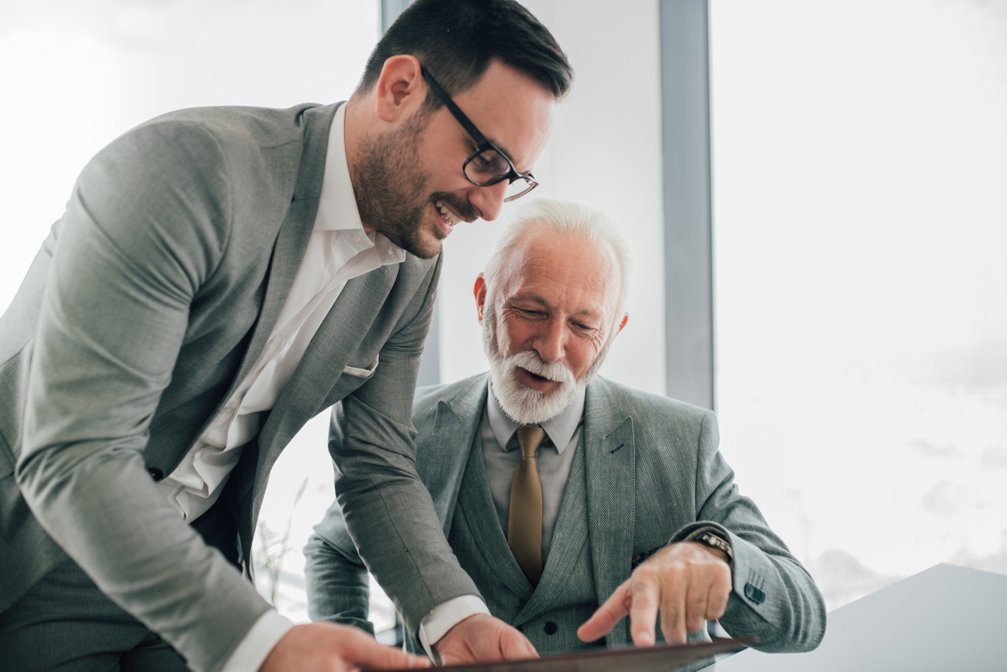 Ein Mann mit Tablet spricht mit einem &auml;lteren Herrn am Tisch.