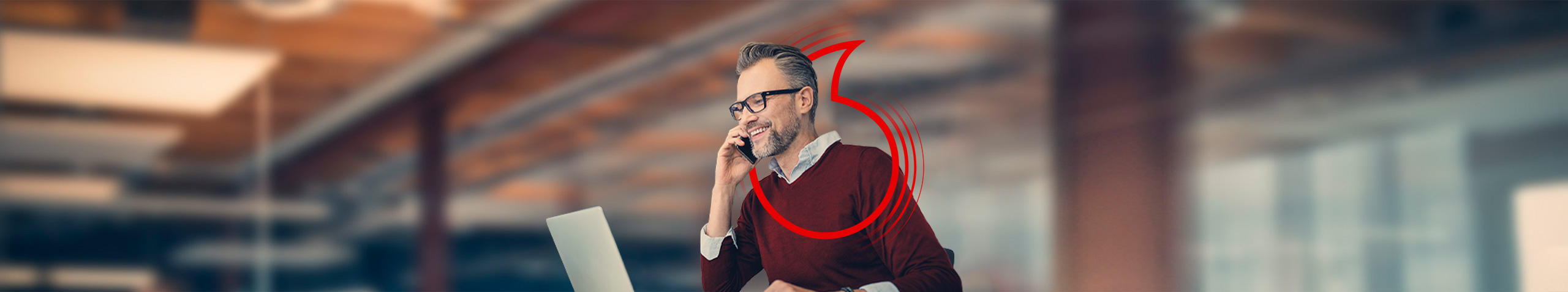 Mann sitzt am Computer und telefoniert.