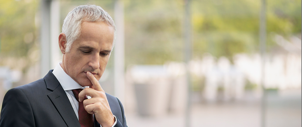 Mann h&auml;lt seinen Finger an den Mund und schaut nachdenklich auf ein Device.