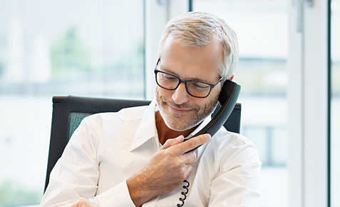 Business-Mann sitzt am Schreibtisch und telefoniert.
