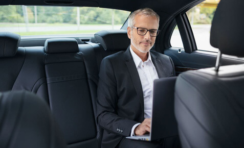 Mann sitzt mit dem Laptop im Auto auf der R&uuml;ckbank und arbeitet.