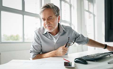 Ein Business-Mann mit Brille in der Hand guckt auf eine Zeichnung auf seinem Schreibtisch. Er nutzt B2B-Kooperationen, die er &uuml;ber Vodafone gefunden hat.