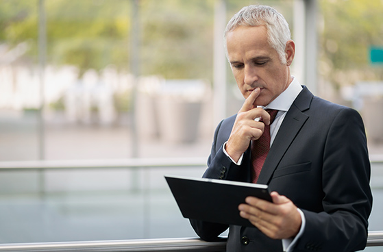 Gesch&auml;ftsmann im Anzug blickt nachdenklich auf sein Tablet