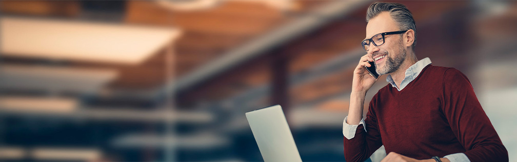 Mann sitzt am Laptop und telefoniert