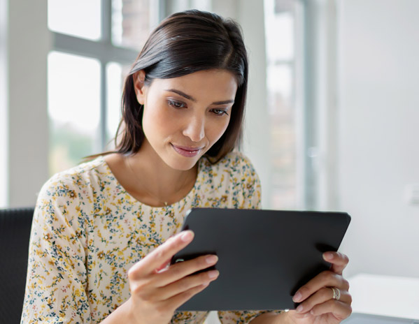 Eine junge Frau sitzt im B&uuml;ro mit hohen Decken und surft auf ihrem Business-Tablet im Internet, um mehr Datenvolumen zu buchen.