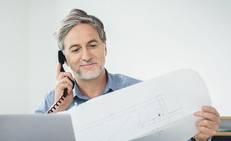 Herr betrachtet einen Bauplan, w&auml;hrend er telefoniert
