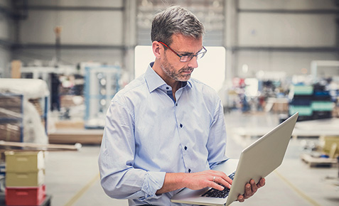 Mann in einer Firmenhalle steuert mit seinem Laptop Prozesse &uuml;ber die Cloud.