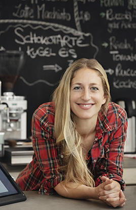 Verk&auml;uferin lehnt im Cafe auf der Ladentheke