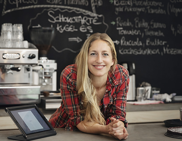 Verk&auml;uferin lehnt im Cafe auf der Ladentheke
