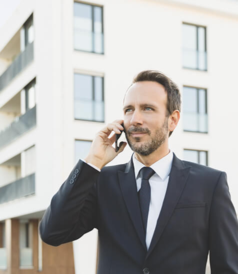 Herr im Anzug steht telefonierend vor einem Hochhaus