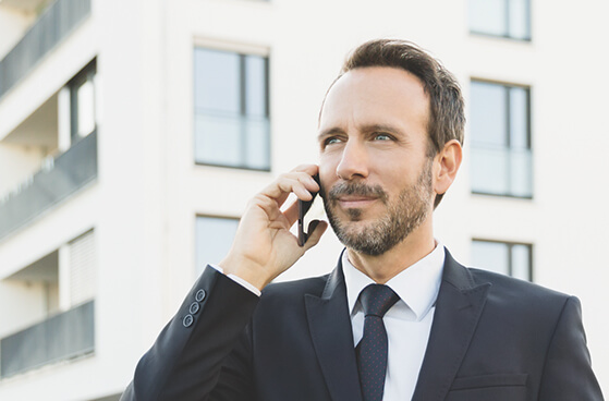 Herr im Anzug steht telefonierend vor einem Hochhaus