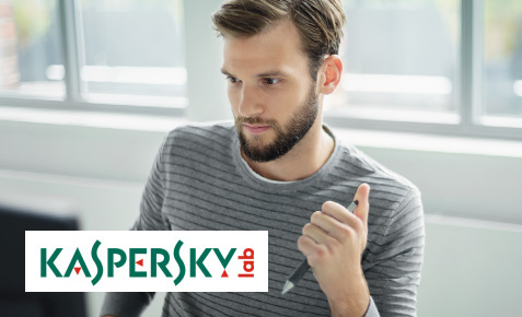 Junger Mann sitzt mit Stift in der Hand am Schreibtisch. Bild mit Kaspersky lab Logo.