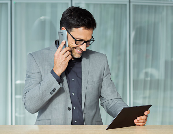 Mann telefoniert und guckt auf sein Tablet.