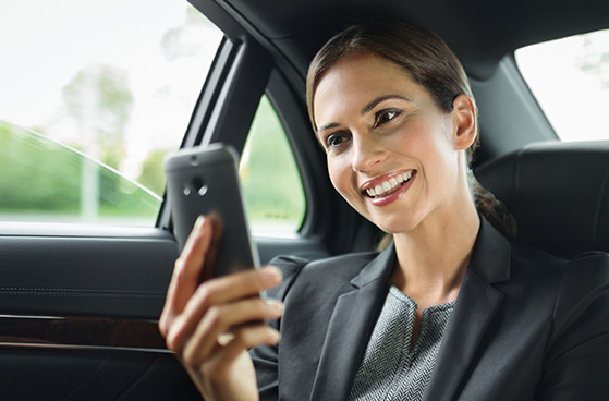 Junge Dame sitzt auf der R&uuml;ckbank im Auto und guckt auf ihr Smartphone