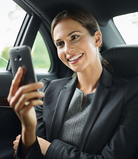 Junge Dame sitzt auf der R&uuml;ckbank im Auto und guckt auf ihr Smartphone