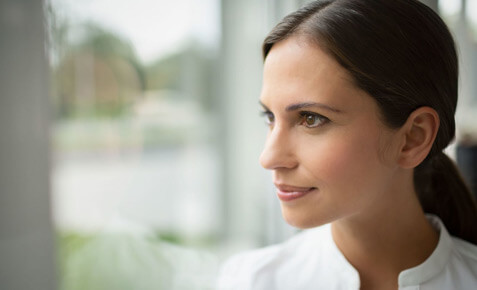 Business-Frau schaut aus dem Fenster und sch&uuml;tzt Ihr Unternehmen mit Vodafone Security vor unautorisiertem Zugriff auf Ihr Netzwerk.