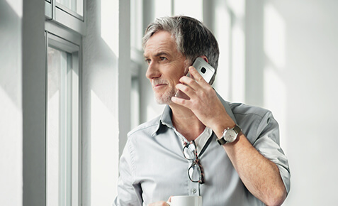 Gesch&auml;ftsmann steht am Fenster und telefoniert mit seinem Red Business Vertrag ins Ausland.