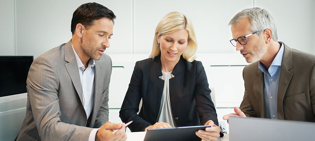 Drei Personen sitzen am Tisch und sprechen &uuml;ber Business-Themen.