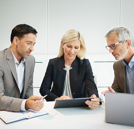 Drei Personen sitzen am Tisch und sprechen &uuml;ber Business-Themen.